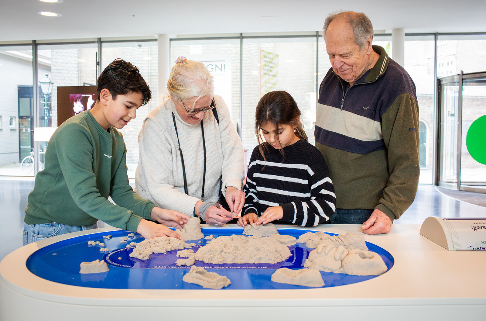 Opa, oma en twee kleinkinderen spelen met magisch zand in het OntwerpStation