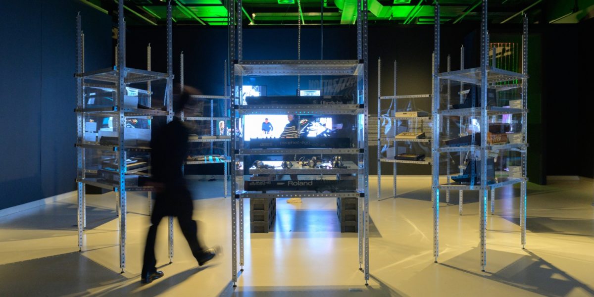 Bezoeker loopt rond in een tentoonstellingszaal vol synthesizers.