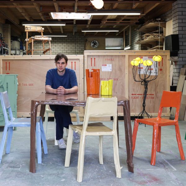 Teun zwets zittend aan een door hem ontworpen tafel in zijn studio omringd door kleurrijke meubels.