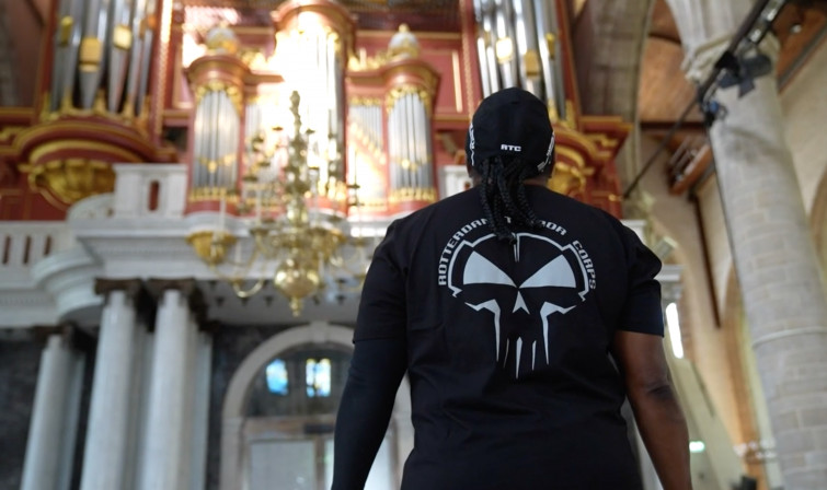 Een man in een t-shirt van Rotterdam Terror Corps staat in een kerk. Hij is van achter gefotografeerd terwijl hij omhoog kijkt naar het orgel van de Laurenskerk.