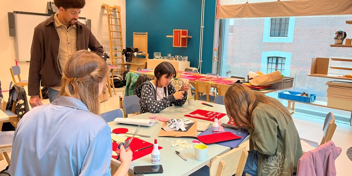 Jongeren zitten rond een tafel en werken samen een een textielwerkstuk.