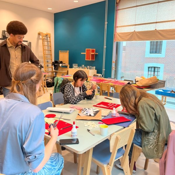 Jongeren zitten rond een tafel en werken samen een een textielwerkstuk.