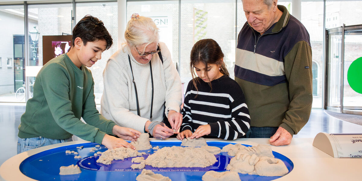 Opa, oma en twee kleinkinderen spelen met magisch zand in het OntwerpStation