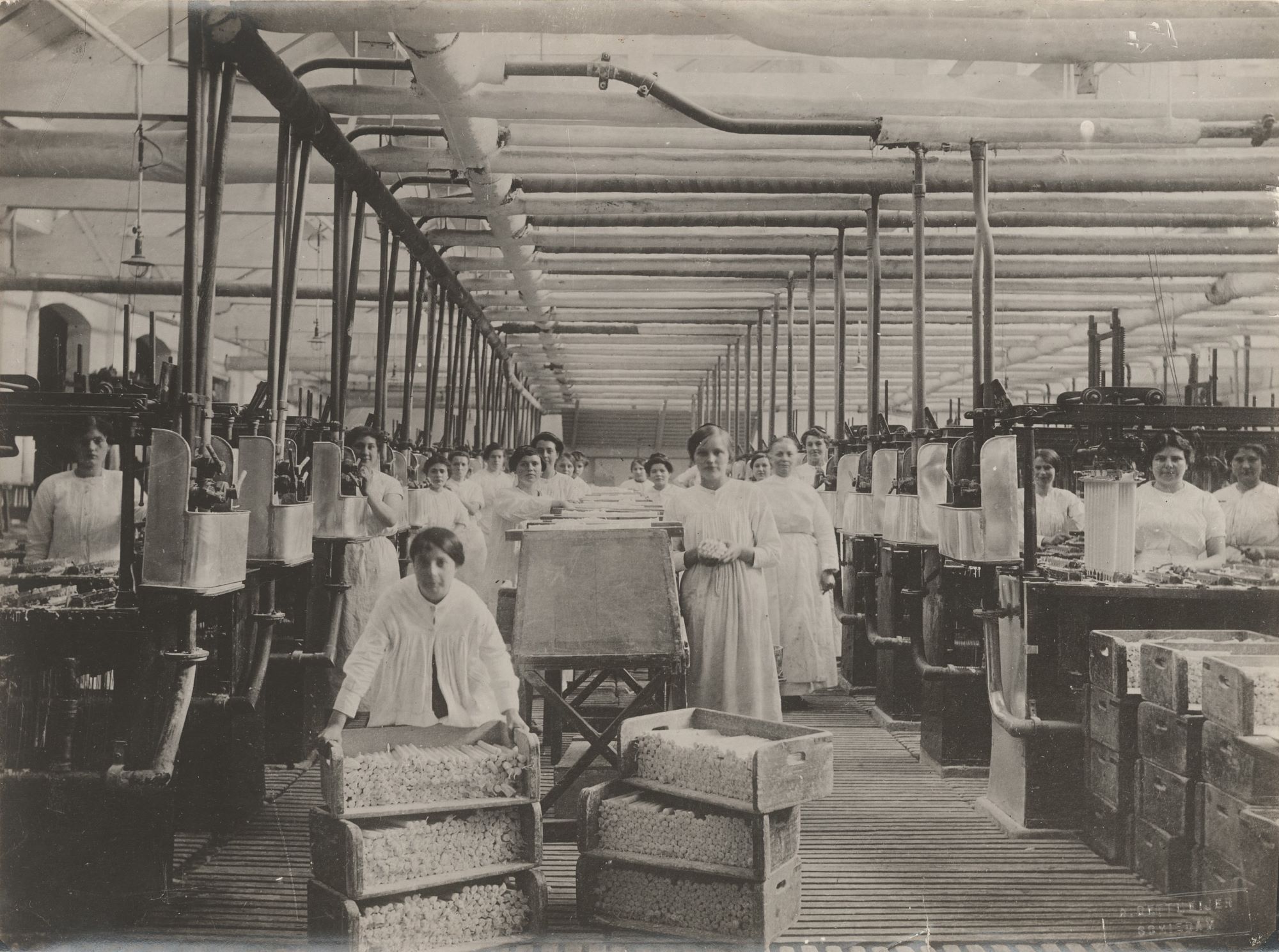 Historische zwart wit foto. Personeel van stearinekaarsenfabriek Apollo aan de Voorhavenkade vervoert kaarsen van de gietkamer naar de opslagruimte.